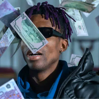 A person wearing sunglasses and a dark jacket is surrounded by various denominations of paper currency falling through the air, illustrating the chaos that can come from neglecting budgeting.