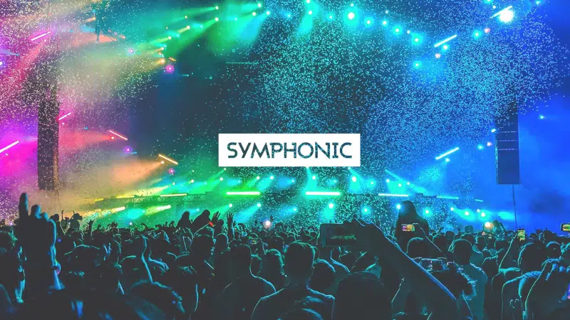 A large crowd at a concert with colorful stage lights and confetti; "SYMPHONIC" is written in bold text at the center.