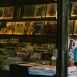 A record store display in CDMX featuring vinyl albums on shelves and stacks of magazines, with a window view of the street outside.