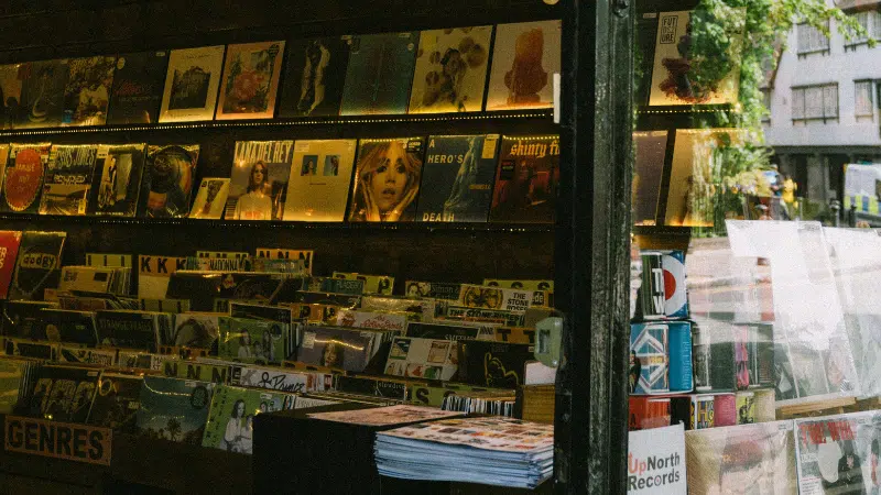 A record store display in CDMX featuring vinyl albums on shelves and stacks of magazines, with a window view of the street outside.