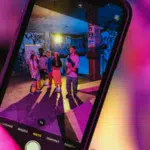 A smartphone screen displays three people posing for a photo in a colorful, graffiti-covered space under vibrant lighting, capturing a moment of joy and connection that celebrates friendship and mental health.