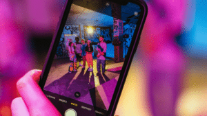 A smartphone screen displays three people posing for a photo in a colorful, graffiti-covered space under vibrant lighting, capturing a moment of joy and connection that celebrates friendship and mental health.