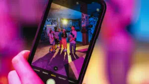 A smartphone screen displays three people posing for a photo in a colorful, graffiti-covered space under vibrant lighting, capturing a moment of joy and connection that celebrates friendship and mental health.