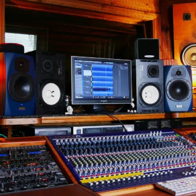 A professional recording studio setup featuring multiple monitors, audio mixing consoles, speakers, and various audio equipment in a wood-paneled room—ideal for artists and label sessions.