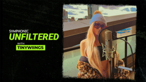 A woman with long blonde hair and sunglasses sings into a microphone on a rooftop. Text reads: "Symphonic Unfiltered with Tinywiings.