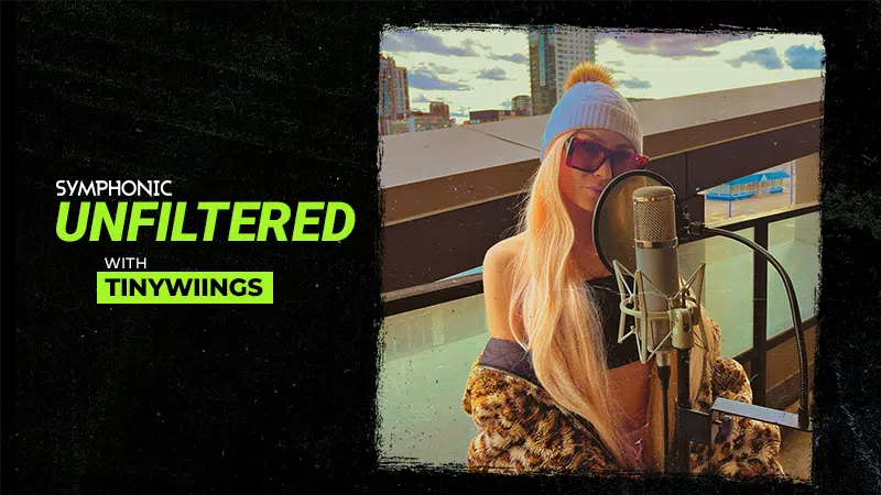 A woman with long blonde hair and sunglasses sings into a microphone on a rooftop. Text reads: "Symphonic Unfiltered with Tinywiings.