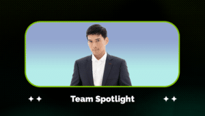 A person in a dark suit and white shirt stands against a blue gradient background, framed by a graphic with the text "Team Spotlight" below.