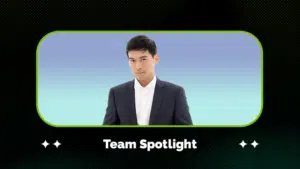 A person in a dark suit and white shirt stands against a blue gradient background, framed by a graphic with the text "Team Spotlight" below.