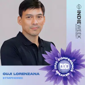 A man with short dark hair and a black shirt poses in front of an AIR Indie Week Australia Edition 2025 Conference Speaker banner, labeled "Guji Lorenzana, Symphonic.