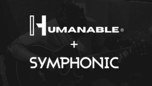 An artist playing an acoustic guitar with the words "HUMANABLE + SYMPHONIC" overlaid in bold white text.