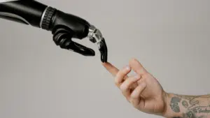 A robotic hand and a human hand reach toward each other, with their fingers nearly touching against a plain background, symbolizing the intersection of technology and humanity in a scene reminiscent of iconic copyright imagery.