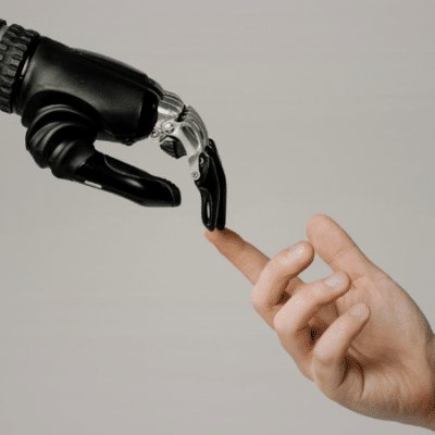 A robotic hand and a human hand reach toward each other, with their fingers nearly touching against a plain background, symbolizing the intersection of technology and humanity in a scene reminiscent of iconic copyright imagery.