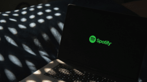 Everything You Need To Know About Spotify Super Listeners A laptop displaying the Spotify logo on its screen sits on a dark surface, surrounded by dappled light patterns that add an atmospheric touch.