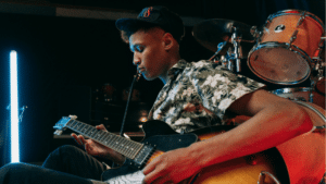 Post-Release Strategies to Maximize Your Track’s Momentum A young man wearing a floral shirt and cap plays an electric guitar on stage, with drums and stage lights in the background, celebrating the release of new music.