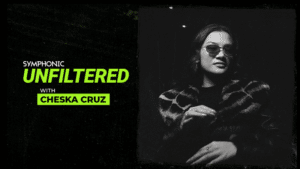 Unfiltered: Full Interview with Cheska Cruz Black and white image with text "Symphonic Unfiltered with Chesk Cruz" next to a woman wearing sunglasses and a patterned coat, standing in a dimly lit setting.