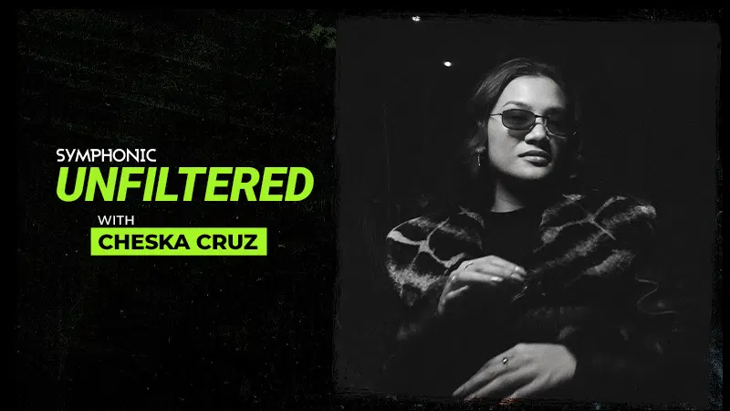 Black and white image with text "Symphonic Unfiltered with Chesk Cruz" next to a woman wearing sunglasses and a patterned coat, standing in a dimly lit setting.