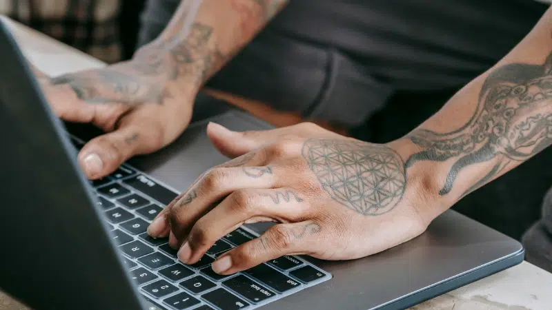 Tattooed hands typing on a laptop keyboard.