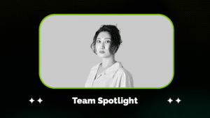 Meet Our Team: Christine Su Black and white portrait of a woman with an updo hairstyle, wearing a collared shirt, framed above the text "Team Spotlight" on a dark patterned background.