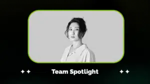 Black and white portrait of a woman with an updo hairstyle, wearing a collared shirt, framed above the text "Team Spotlight" on a dark patterned background.