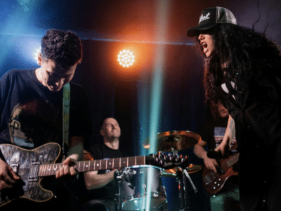 A rock band performs on stage with a guitarist, drummer, bassist, and a vocalist in a hat singing passionately under colorful stage lights, drawing the crowd into their energetic fan funnel.