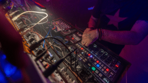 A distributor expertly operates a variety of electronic music equipment and synthesizers, illuminated by colorful stage lighting.