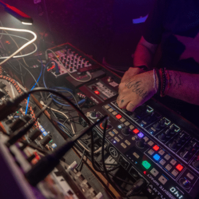A distributor expertly operates a variety of electronic music equipment and synthesizers, illuminated by colorful stage lighting.