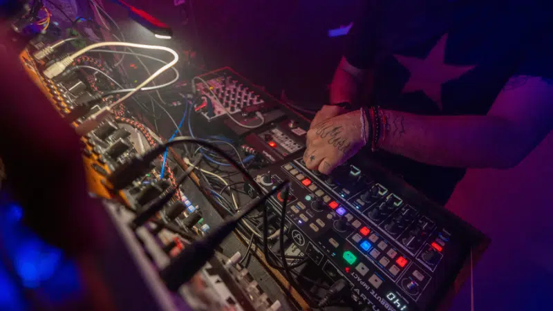 A distributor expertly operates a variety of electronic music equipment and synthesizers, illuminated by colorful stage lighting.