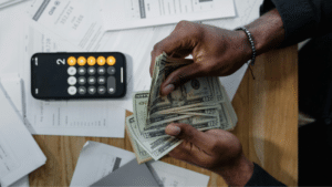 Why Symphonic’s SplitShare Feature Outshines the Competition in Royalty Splitting A person counts US dollar bills at a desk with a calculator, scattered financial documents, and the SplitShare app open on their screen.
