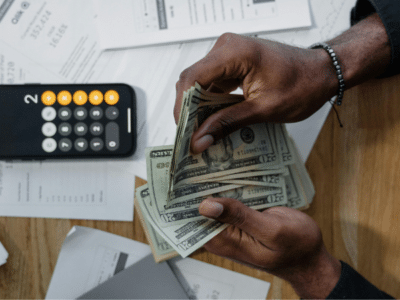 A person counts US dollar bills at a desk with a calculator, scattered financial documents, and the SplitShare app open on their screen.