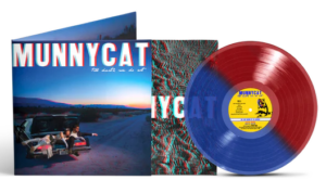 A red and blue vinyl record with a yellow center label is displayed alongside its cover featuring the text "MUNNYCAT" and an image of a car on a deserted road at dusk.