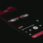 A smartphone screen in a dark setting displays the Spotify music player interface with a song titled "LoveYou" currently playing.
