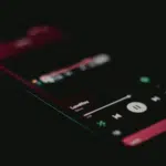 A smartphone screen in a dark setting displays the Spotify music player interface with a song titled "LoveYou" currently playing.