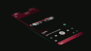 A smartphone screen in a dark setting displays the Spotify music player interface with a song titled "LoveYou" currently playing.