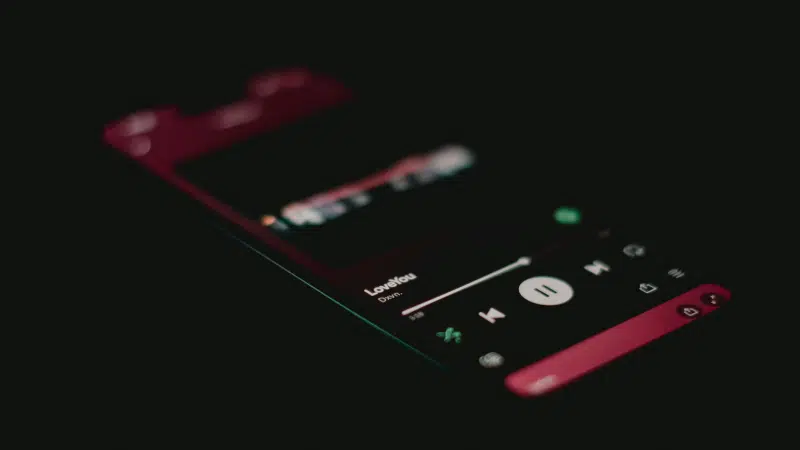 A smartphone screen in a dark setting displays the Spotify music player interface with a song titled "LoveYou" currently playing.