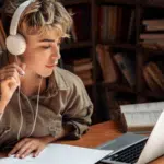 Tips For Independent Artists Looking To Distribute CDs and Vinyl A person with headphones studies at a desk, immersed in symphonic tunes, surrounded by a laptop, notebook, open book, and coffee cup in a quiet library or study room.