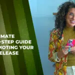 A woman with curly hair and glasses stands holding a phone next to a sign reading "The Ultimate Step-By-Step Guide to Promoting Your Music Release.