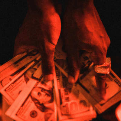 A person wearing a ring holds several spread-out U.S. $100 bills under red lighting, capturing the vibe of success often associated with the music distribution industry.