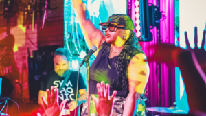 A performer on stage raises one arm while singing into a microphone, capturing the excitement of getting started as colorful lights shine and the audience raises their hands in the foreground.