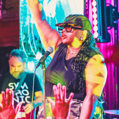 A performer on stage raises one arm while singing into a microphone, capturing the excitement of getting started as colorful lights shine and the audience raises their hands in the foreground.