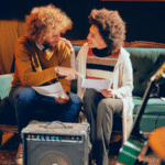 Top Features Artists Love in DSPs and Why They Matter in 2025 Two people sit on a green couch, holding papers and talking about DSPs amid musical instruments, including guitars and a keyboard, in a cozy, dimly lit room.