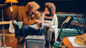 Top Features Artists Love in DSPs and Why They Matter in 2025 Two people sit on a green couch, holding papers and talking about DSPs amid musical instruments, including guitars and a keyboard, in a cozy, dimly lit room.