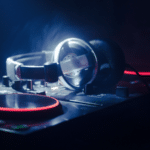 A pair of headphones rests on a DJ mixer with illuminated red and orange lights in a dimly lit environment, setting the scene for some serious playlist pitching.
