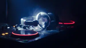 A pair of headphones rests on a DJ mixer with illuminated red and orange lights in a dimly lit environment, setting the scene for some serious playlist pitching.