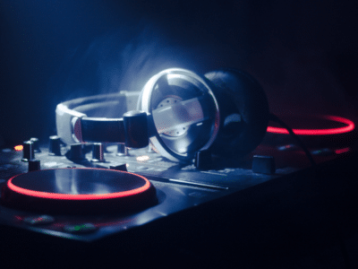 A pair of headphones rests on a DJ mixer with illuminated red and orange lights in a dimly lit environment, setting the scene for some serious playlist pitching.