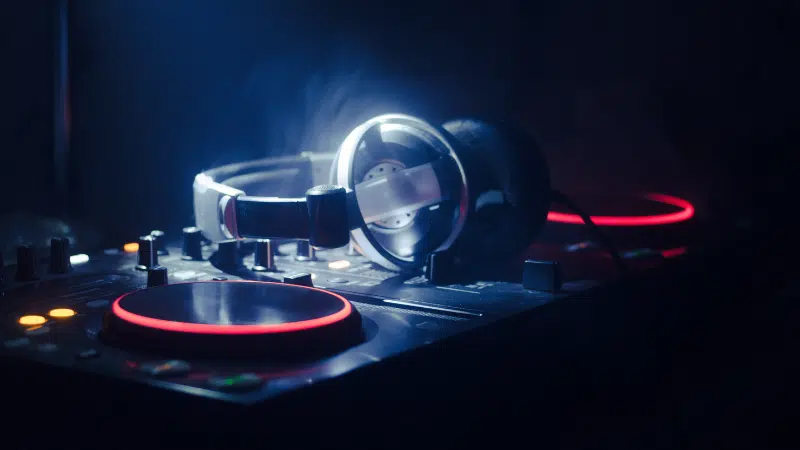 A pair of headphones rests on a DJ mixer with illuminated red and orange lights in a dimly lit environment, setting the scene for some serious playlist pitching.