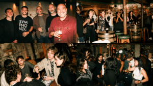 A group of people socialize and enjoy drinks at a lively indoor bar with rustic decor, wooden barrels, and dim lighting.