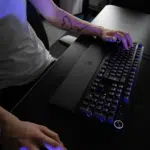 A person using a mechanical keyboard and mouse on a black desk; only their arms and torso are visible.