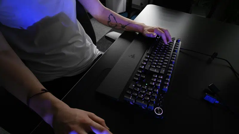 A person using a mechanical keyboard and mouse on a black desk; only their arms and torso are visible.