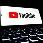 A tablet displaying the YouTube for Artists logo rests above an illuminated computer keyboard in a dark environment.