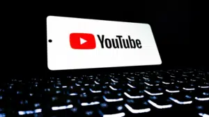 A tablet displaying the YouTube for Artists logo rests above an illuminated computer keyboard in a dark environment.